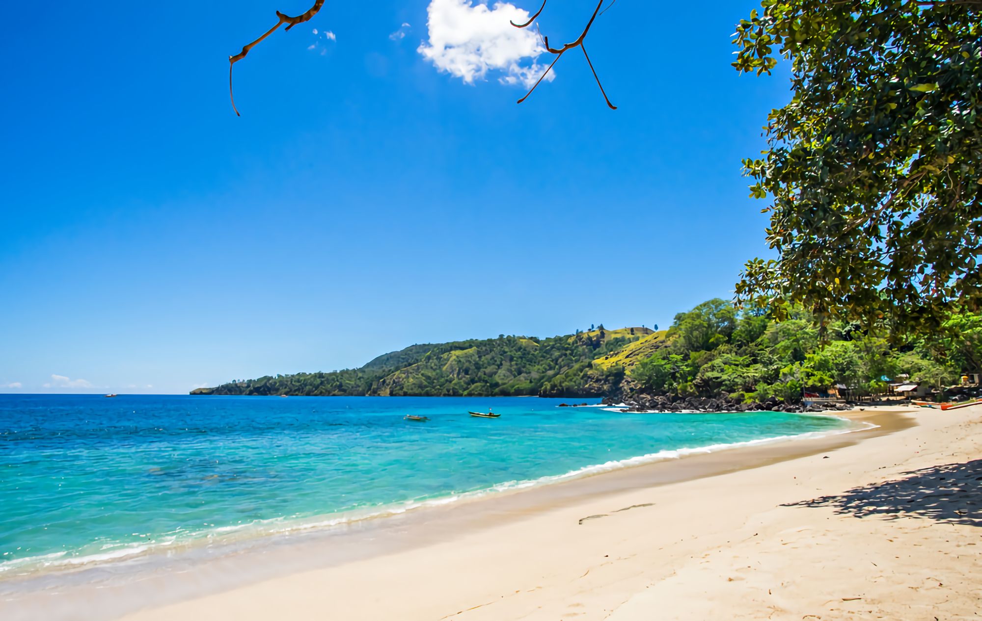 Panorama aerial Pantai Pulisan di Likupang dengan perairan biru toska, pasir putih, dan perbukitan hijau yang mengelilingi teluk.