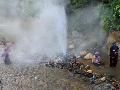 Semburan air panas setinggi tiga meter dari geyser di Pemandian Cipanas Cisolok, Pelabuhan Ratu, dengan latar belakang pepohonan hijau dan kabut tipis.