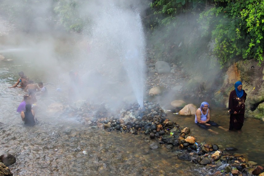 Semburan air panas setinggi tiga meter dari geyser di Pemandian Cipanas Cisolok, Pelabuhan Ratu, dengan latar belakang pepohonan hijau dan kabut tipis.