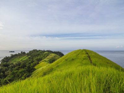 Pulau Diyonumo di Gorontalo Utara menyuguhkan hamparan rumput hijau di puncak bukit. Pulau perawan tanpa fasilitas wisata ini bisa dicapai dengan kapal nelayan/Foto: Indonesia Kaya